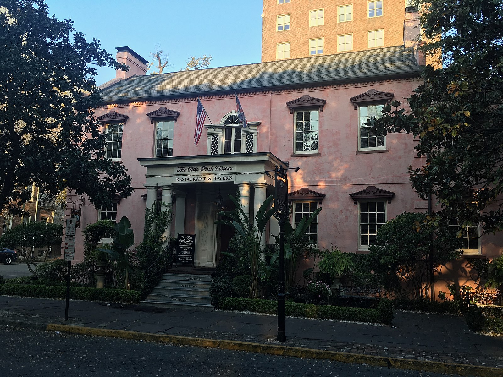 The facade of the Olde Pink House flanked by trees and landscaping.